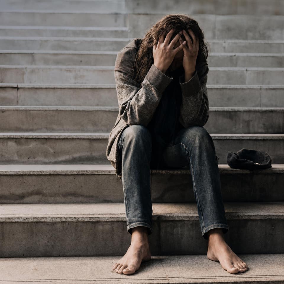 A person sits alone on concrete steps with their face in their hands